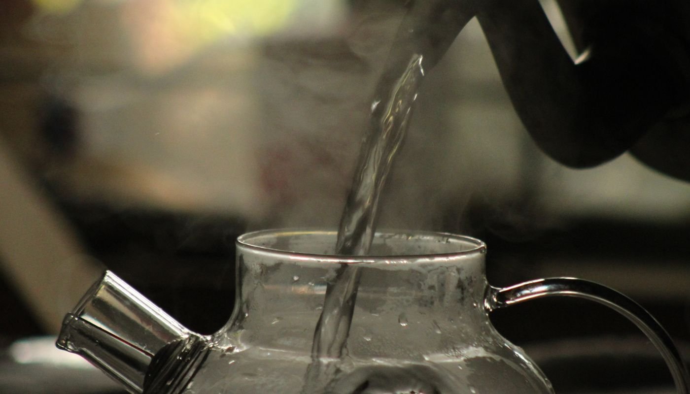 Hot water being poured into a glass pot, steam rising from it
